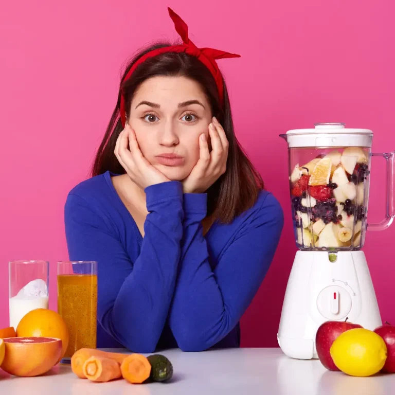 Vrouw kijkt gefrustreerd naar blender vol fruit, omringd door groenten en sapjes, twijfelend over gezond eten